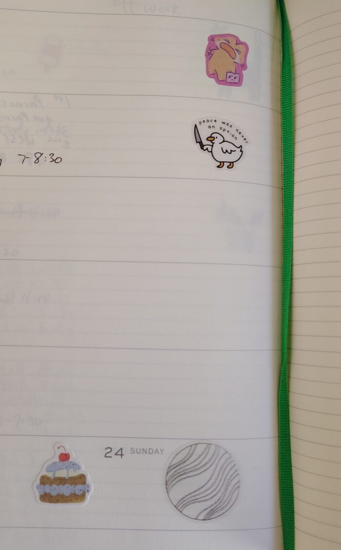 stickers in my planner featuring a duck with a knife, a cartoon cat sobbing, a fancy cake, and a silvery planet