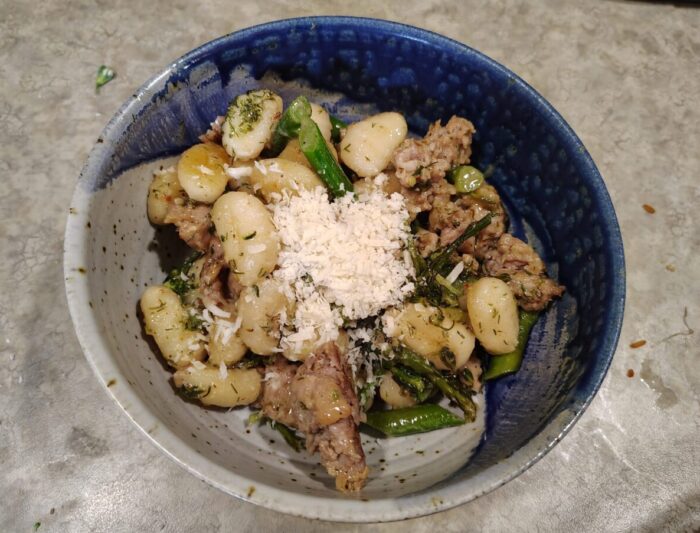 a bowl of gnocchi with sausage and broccolini topped with a little pile of parmesan