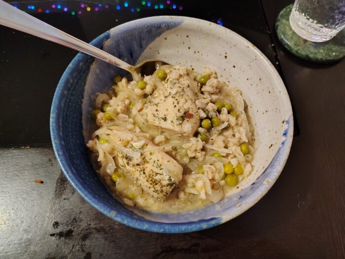 a bowl of an anemic-looking stewy pile of barley, onion, and peas with herbed chunks of chicken on top