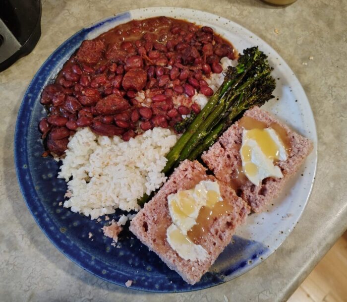 a plate of red beans and rice with broccolini and purple cornbread