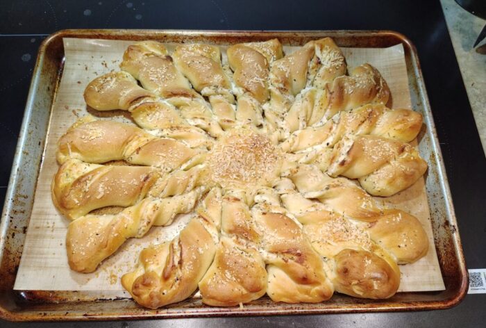 a bread with a round center and twisted pieces radiated outwards. Cheesy filling is visible in the twists and it's all dusted with herbs and parmesan
