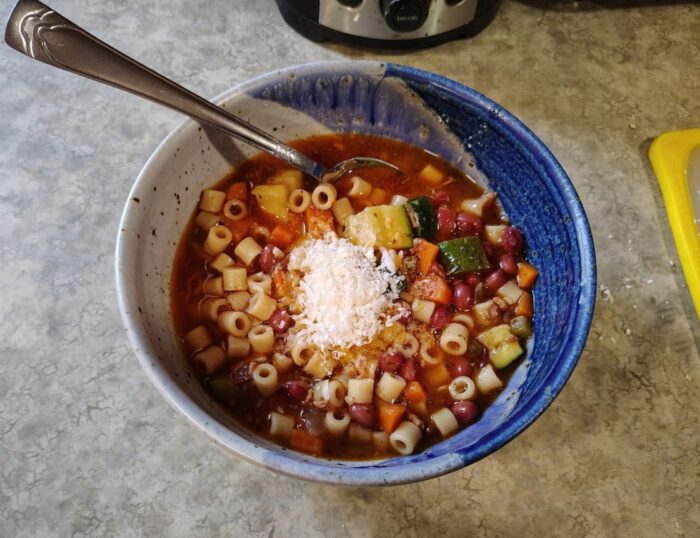 a bowl of bean and noodle soup with chunks of carrots and zucchini, topped with parmesan