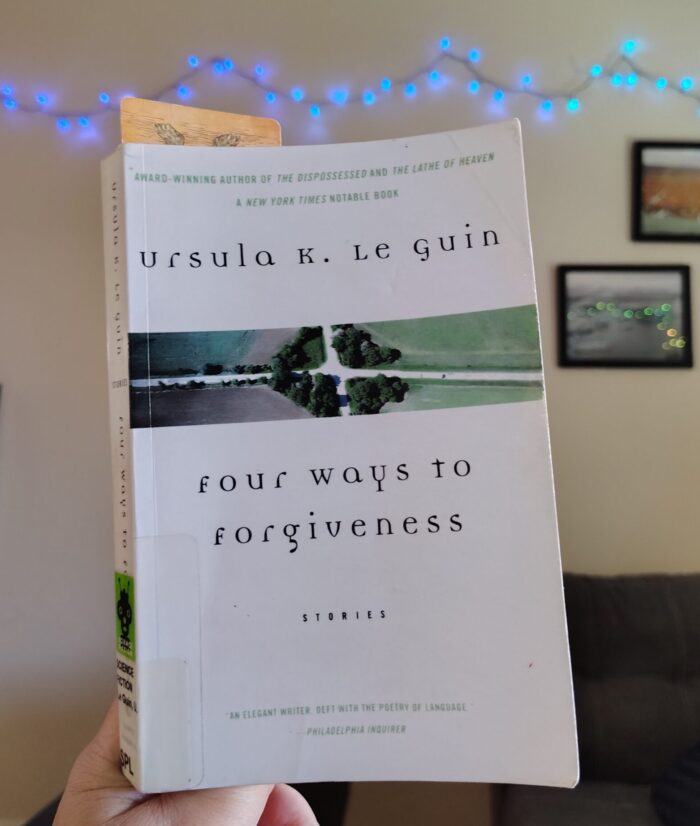 paperback book: Four Ways to Forgiveness. The cover is very boring and mostly white with a small picture of a crossroads