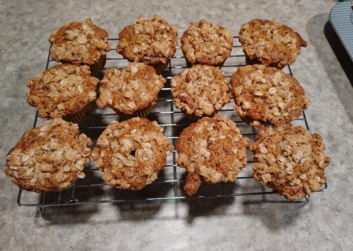 12 muffins cooling on a wire rack. They are golden with crumbly oat streusel on top