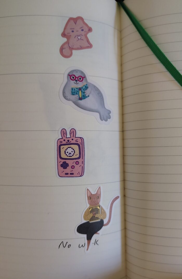 Stickers in my planner featuring an angry cartoon cat, a seal reading a book, a gameboy stylized with bunny ears, and a cat holding a book