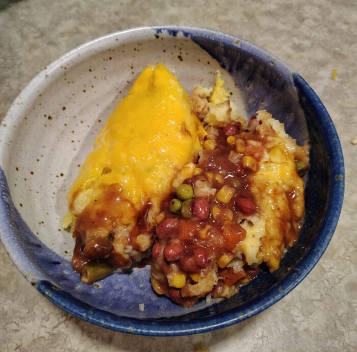 a bowl of beans and vegetables in brown gravy, topped with mashed potatoes and cheese