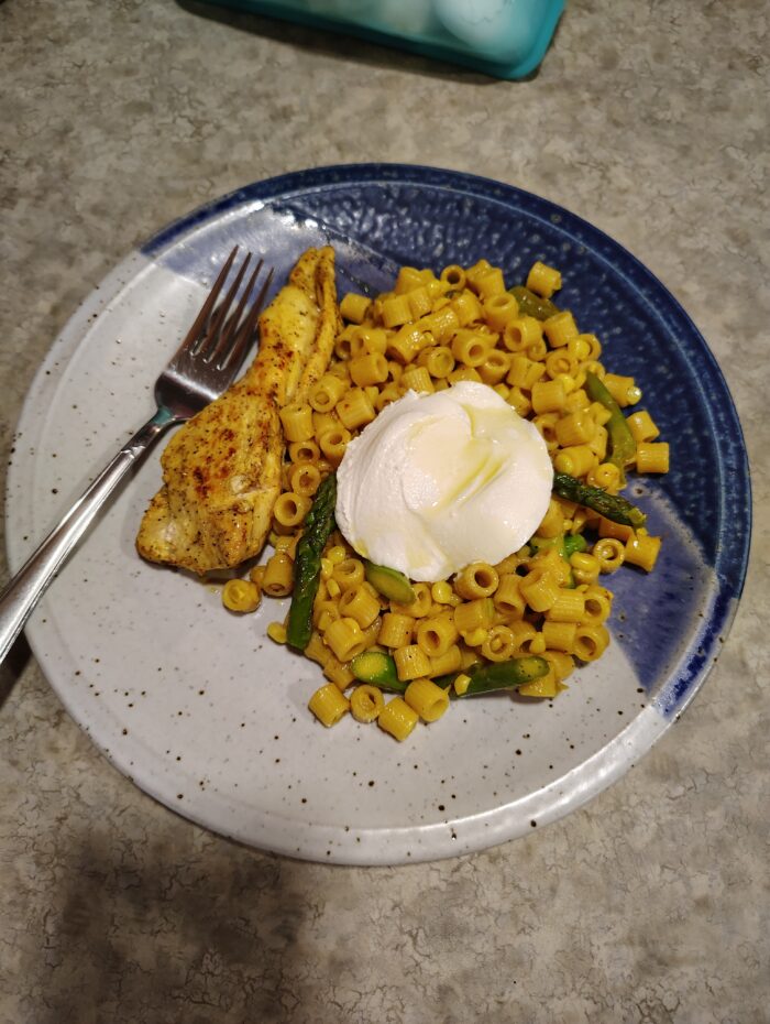 a plate of datilini pasta mixed with corn and asparagus and topped with a big dollop of ricotta. There's some chicken on the side