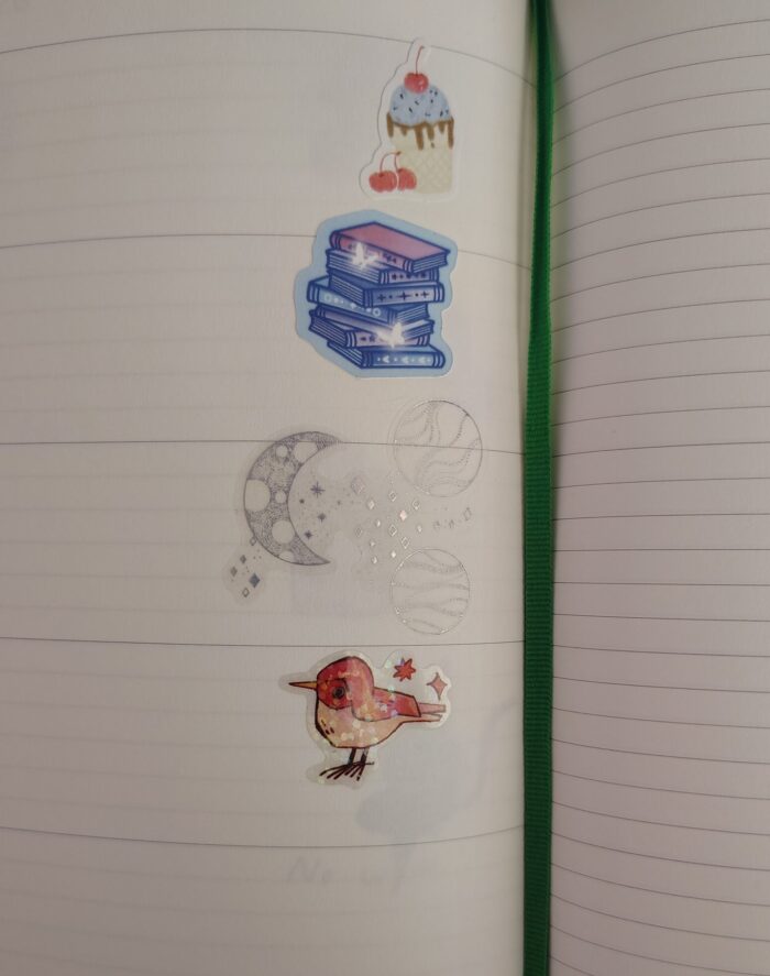 stickers in my planner featuring an ice cream sundae, a magical book pile, sparkly moons, and a glittery little bird