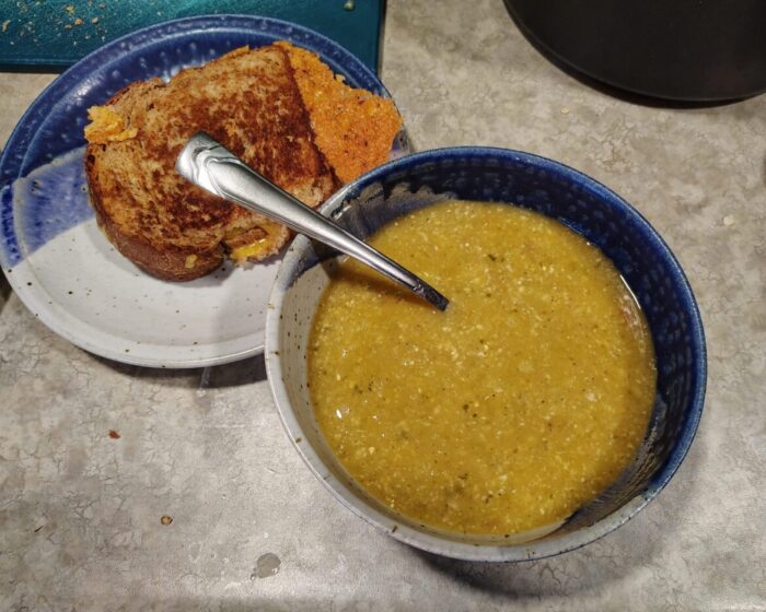 a bowl of corn soup alongside a grilled cheese