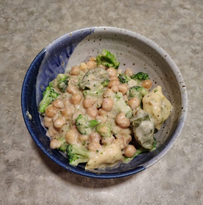 a bowl of chickpeas, tortellini, and broccoli in creamy sauce