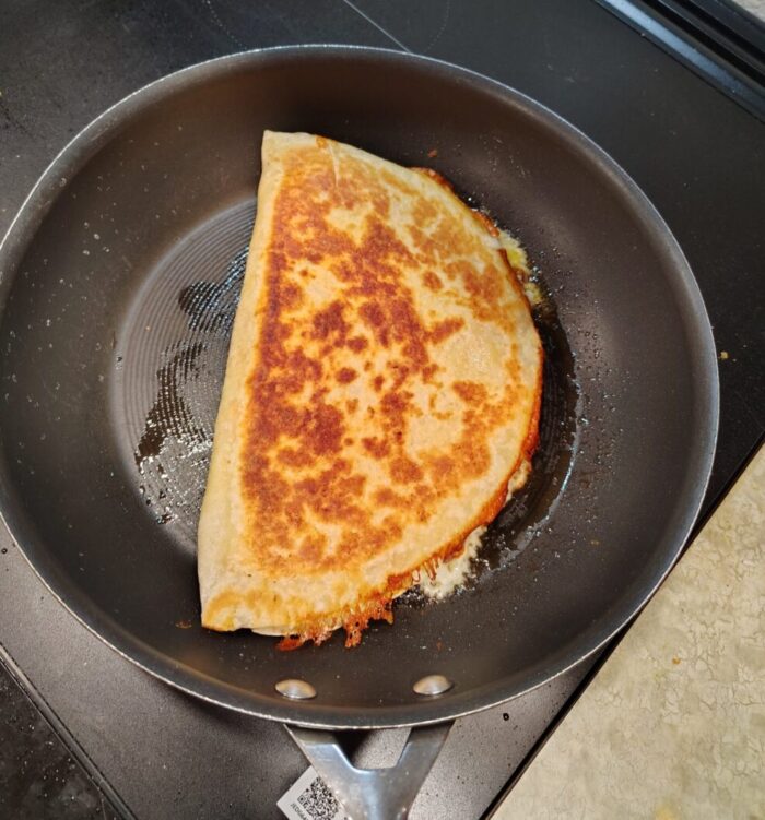 a delightfully browned and oozing quesadilla cooking in a frying pan