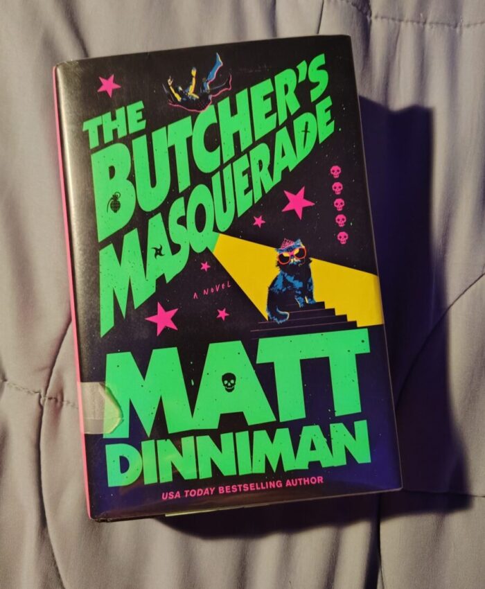 book: The Butcher's Masquerade. Cover features the cat Princess Donut wearing a tiara, sunglasses, and a wireless mic