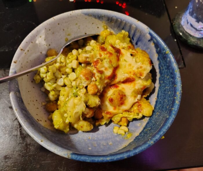 a bowl of corn, gnocchi, and chickpeas with pesto, topped with melty cheese