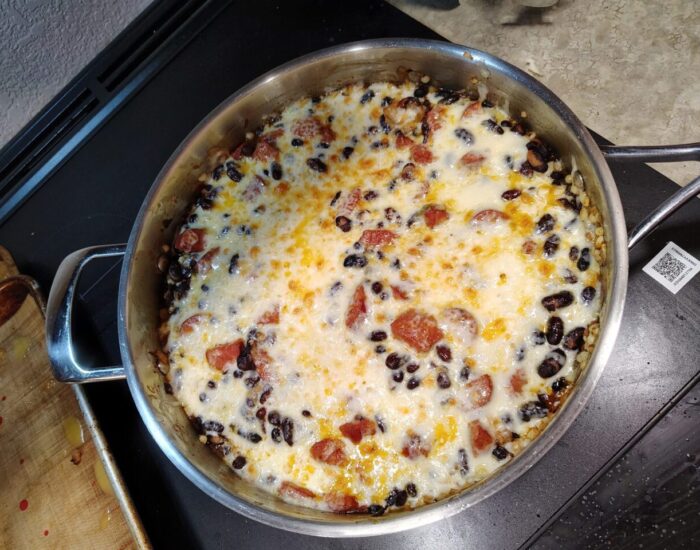 a skillet of beans, corn, and sausage baked with a bunch of cheese on top