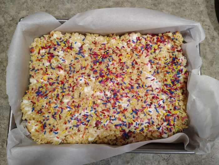 a pan of rice krispie treats with mini marshmallows studded throughout and topped with colorful sprinkles