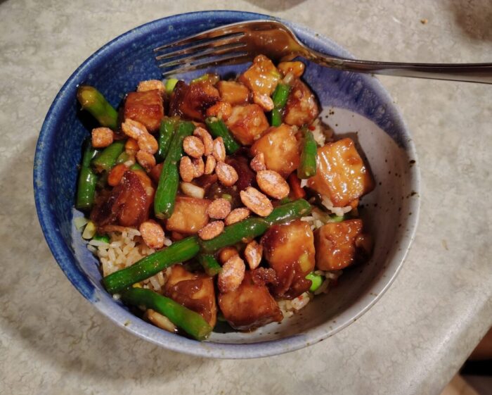 a bowl of tofu and green beans in a glossy sauce on top of rice
