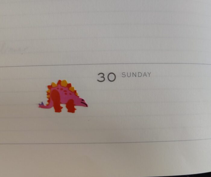 a pink and orange stegosaurus sticker in my planner