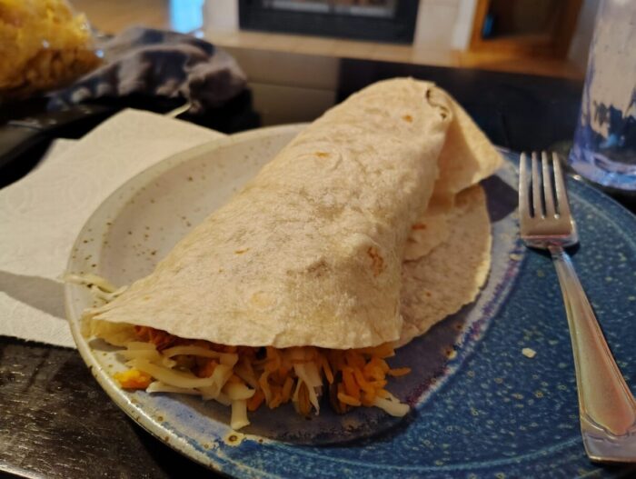 a fat burrito on the plate with rice and cheese spilling out the top