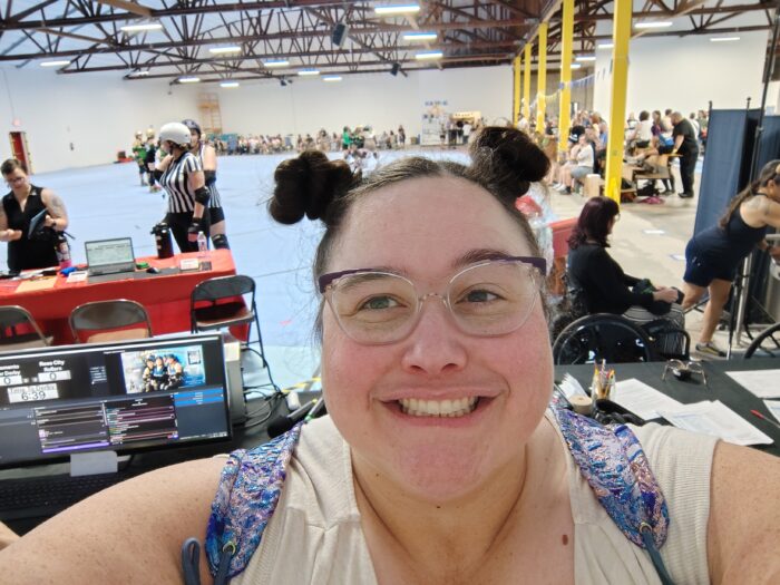me, smiling at the camera, with the announcer table and derby track behind me