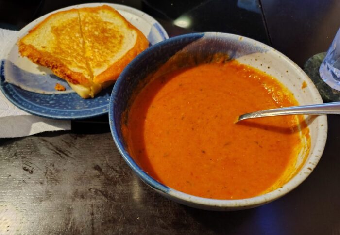 a bowl of tomato soup and a small plate with a grilled cheese sandwich cut on the diagonol