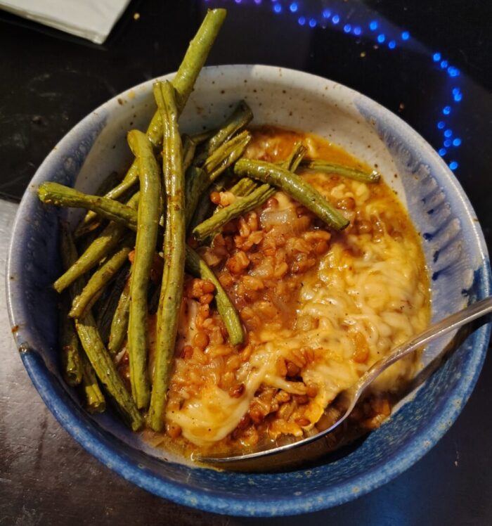 a bowl of stew-y lentils and barley topped with melted cheese, along with some roasted green beans