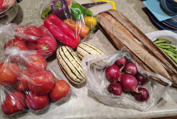 two bags of tomatoes, a bag of peppers, green onions, delicatta squash, green beans, and a baguette