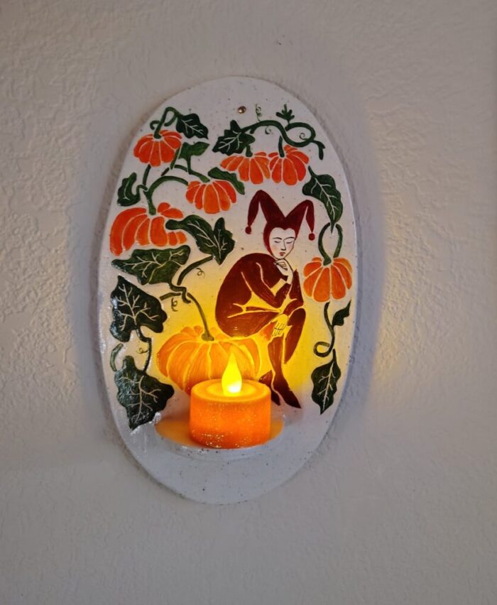 a small ceramic sconce decorated with a jester seated on a pumpkin. There is a glittery orange tea light on its shelf