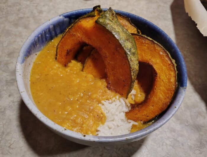 a bowl of rice topped with a yellow split pea stew and slices of roasted kabocha squash